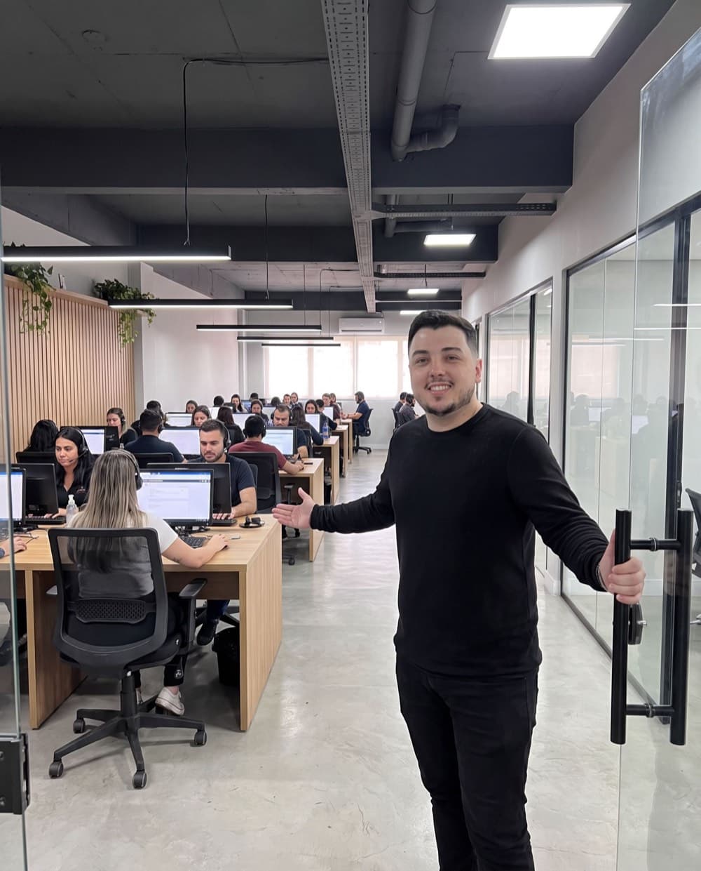 Jeferson Isaías na entrada do salão de operação, com o time da CallSeller atendendo ao fundo